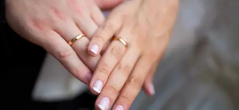 Novomanželé společně ukazují své zlaté snubní prsteny.